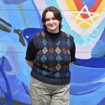 Person wearing a sweater with diamond patterns standing in front of a brightly painted wall